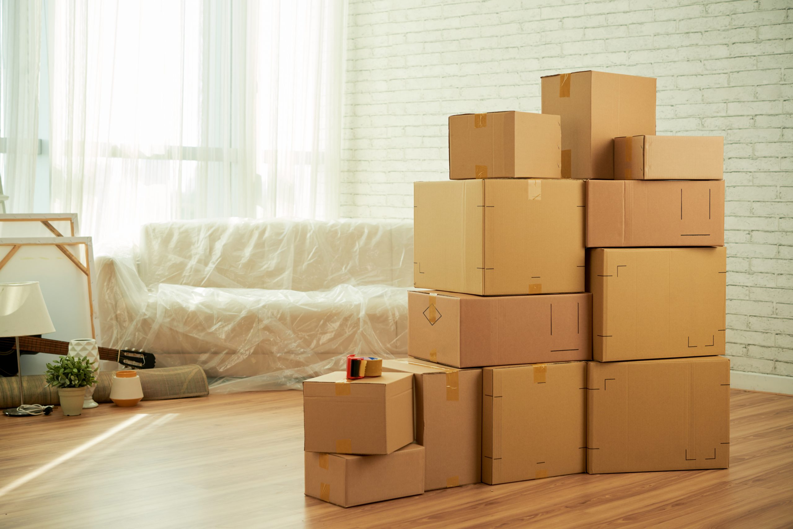 shot-room-interior-with-package-boxes-standing-middle-sofa-covered-with-film Sfeerafbeeldingverhuisbedrijf in Eindhoven en omgeving. Woonkamer met verhuisdozen